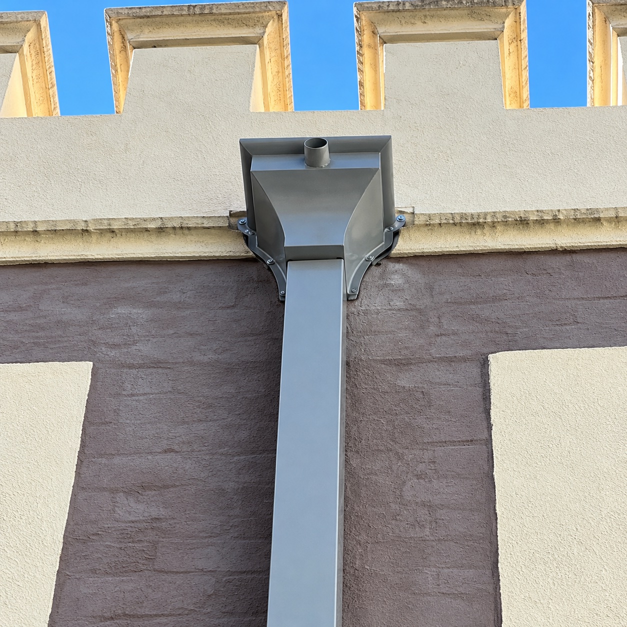 Close-up of a metal rainhead connected to a rectangular downpipe